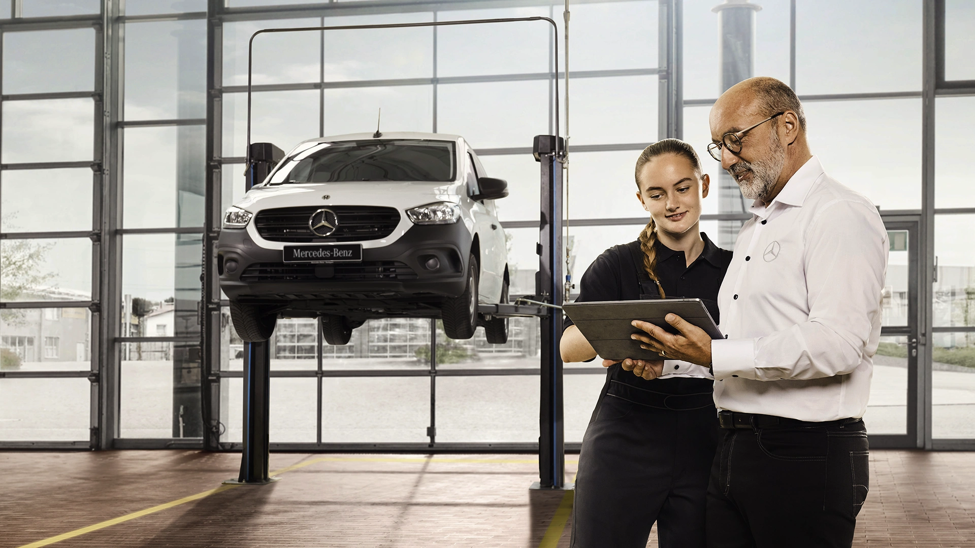 Serviso priėmėjas su kliente servise, fone ant keltuvo furgonas