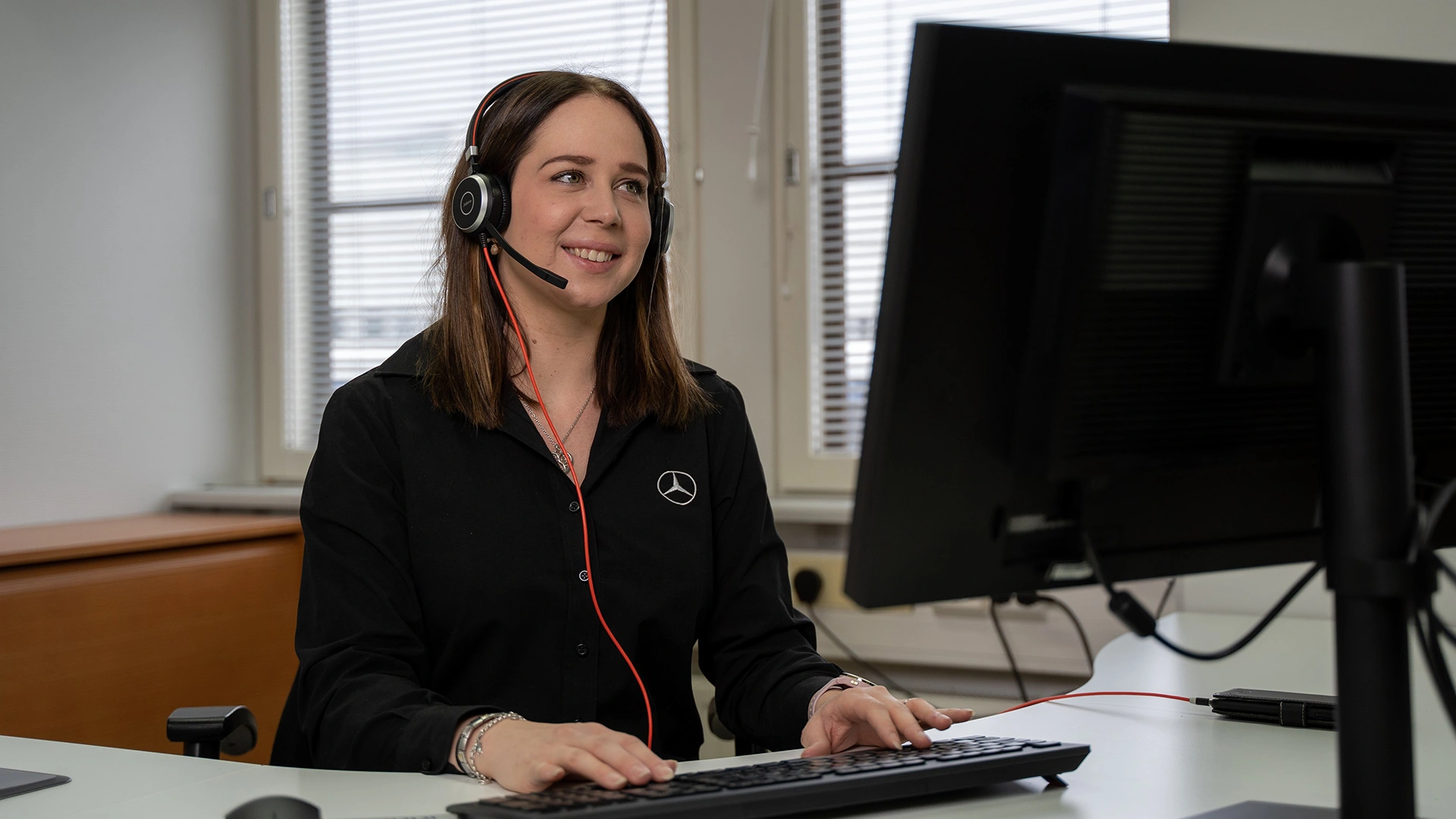 Moteris, dirbanti klientų aptarnavimo srityje, sėdi prie kompiuterio su ausinėmis.