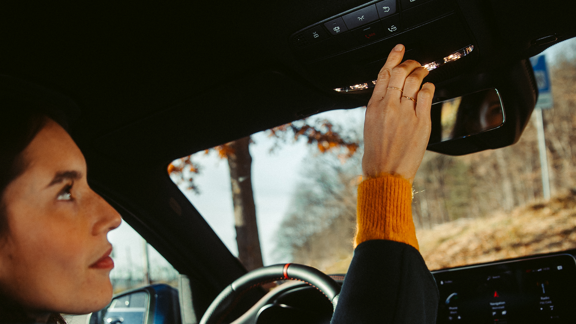 Nainen auton sisällä painamassa kattoyksikön nappia.