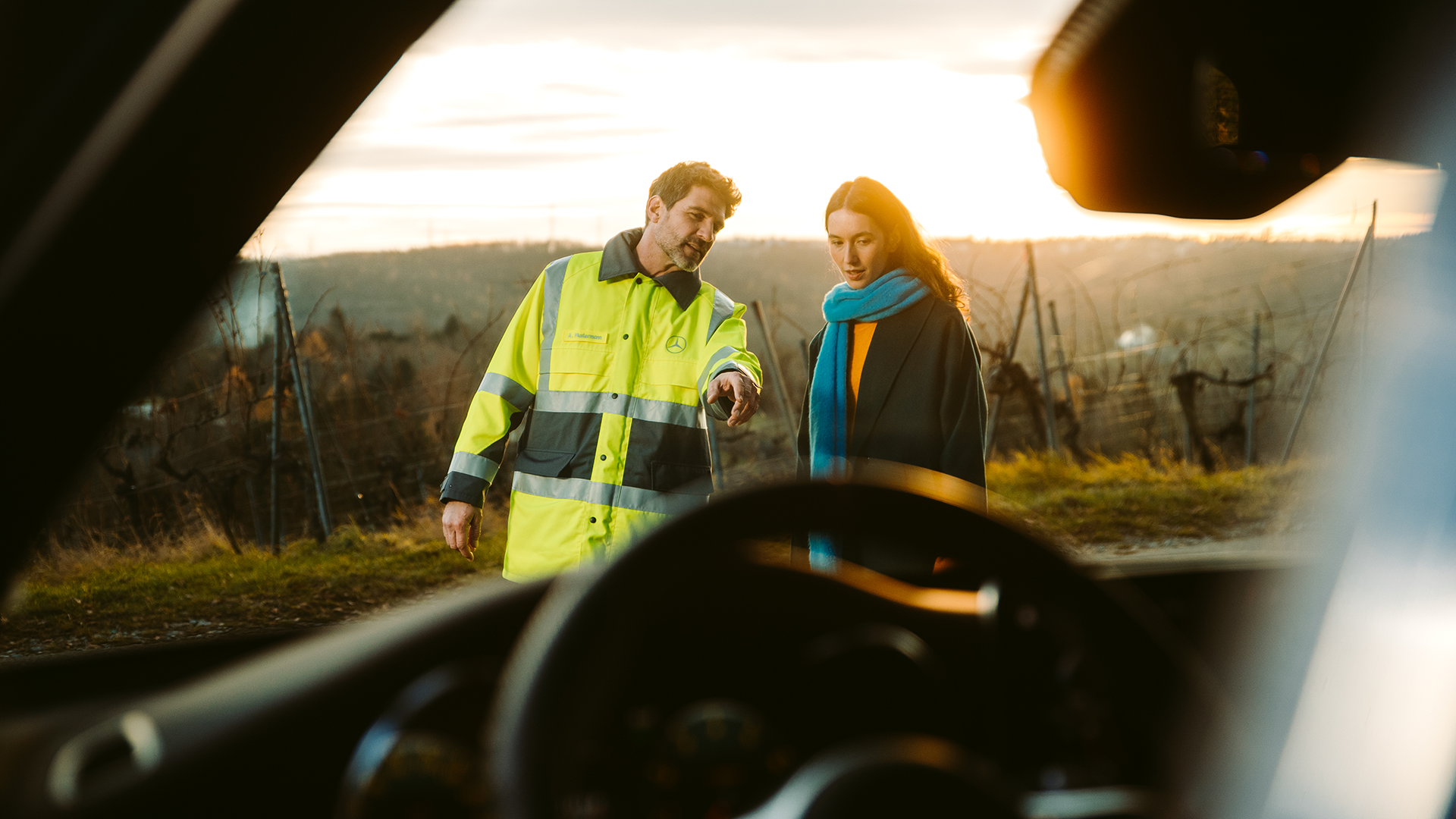 Mercedes kelių serviso mechanikas kalbasi su klientu už automobilio.
